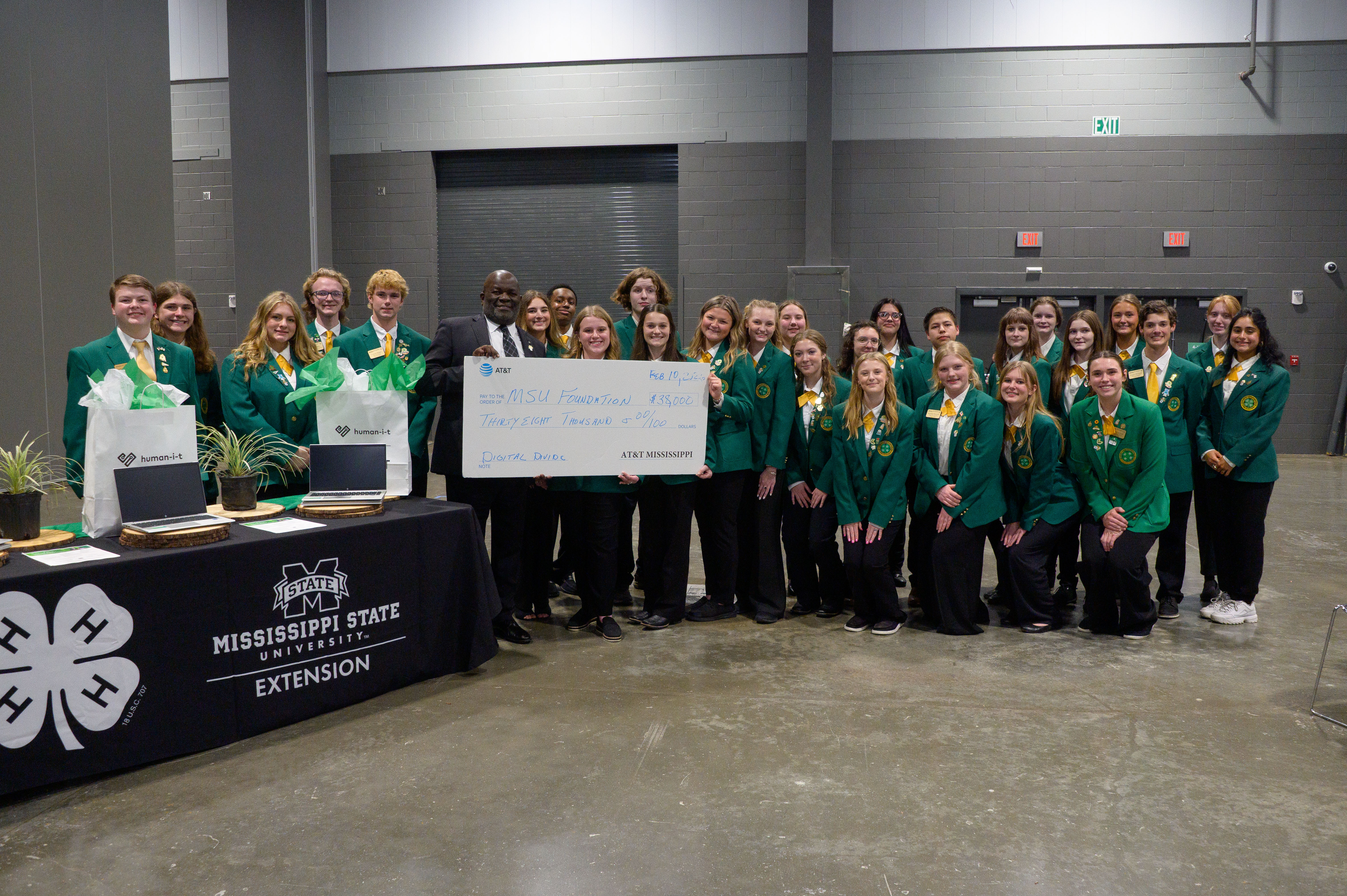 Four people hold a large presentation check for $38,000 to the MSU Foundation as several smiling teens stand around them.