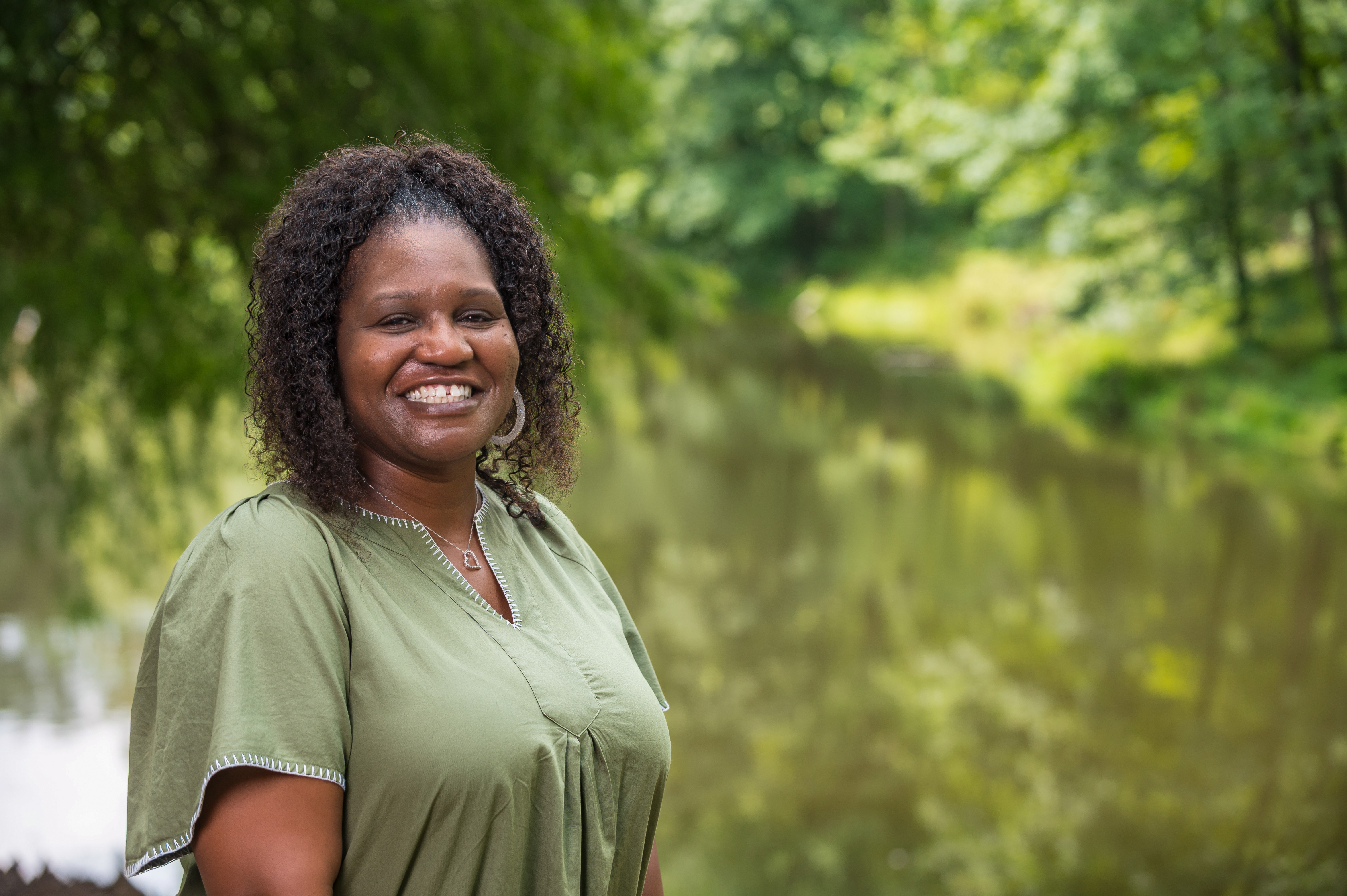 A person standing in front of a pond smiles at the camera.