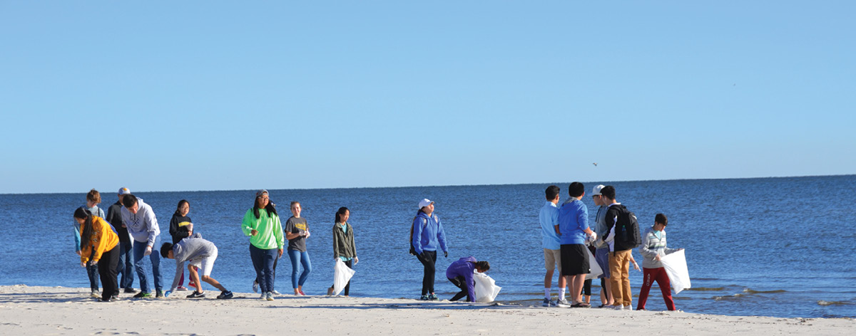 A group of people pick up debris on a beach.