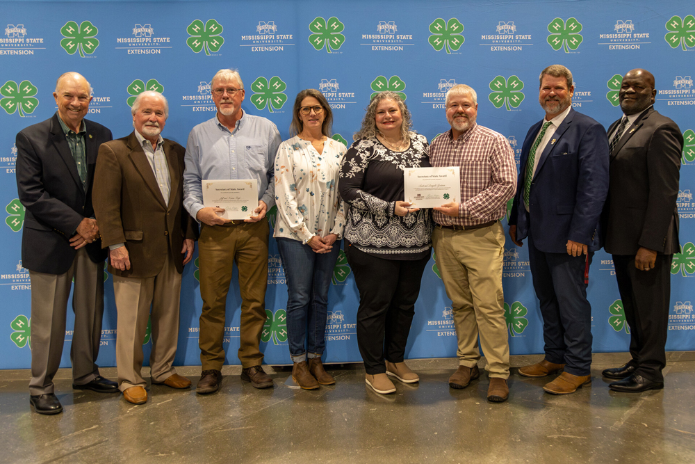 Eight adults stand smiling in front of a 4-H and MSU Extension backdrop.