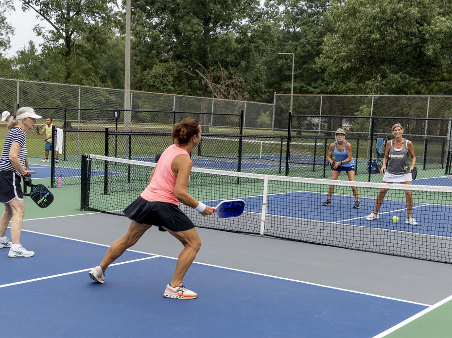 Four women holding paddles play a game on a court.