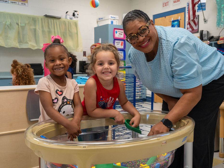 A smiling adult with two smiling children at a bead and building station.