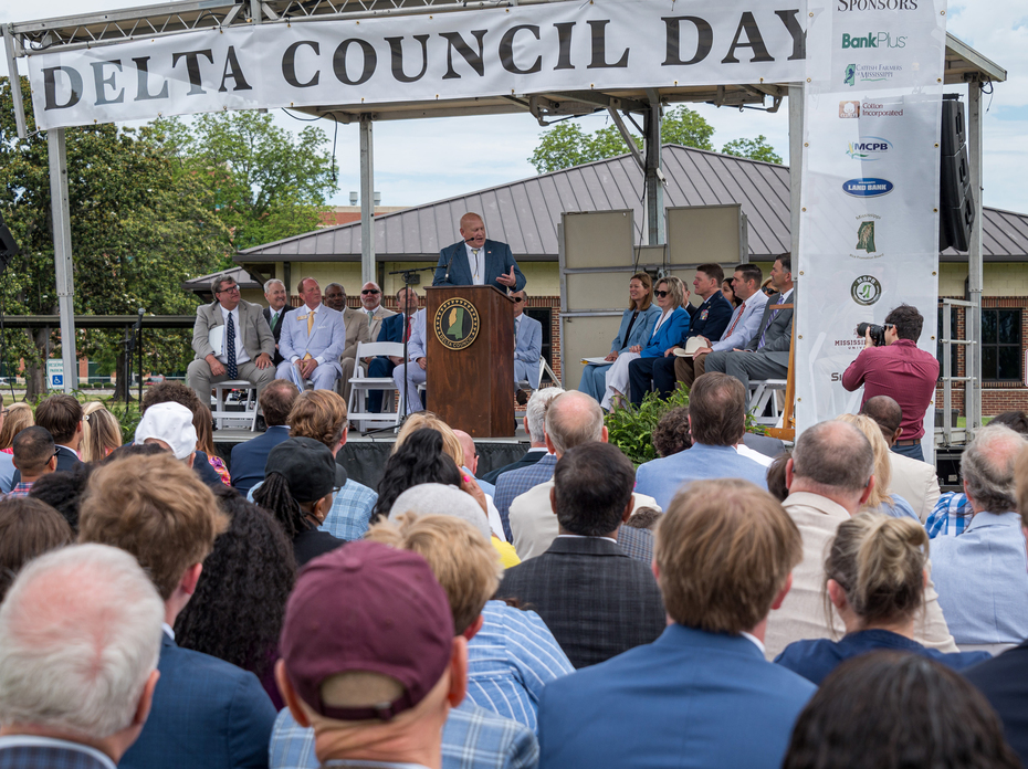 A man speaks to a large crowd from an outdoor stage.
