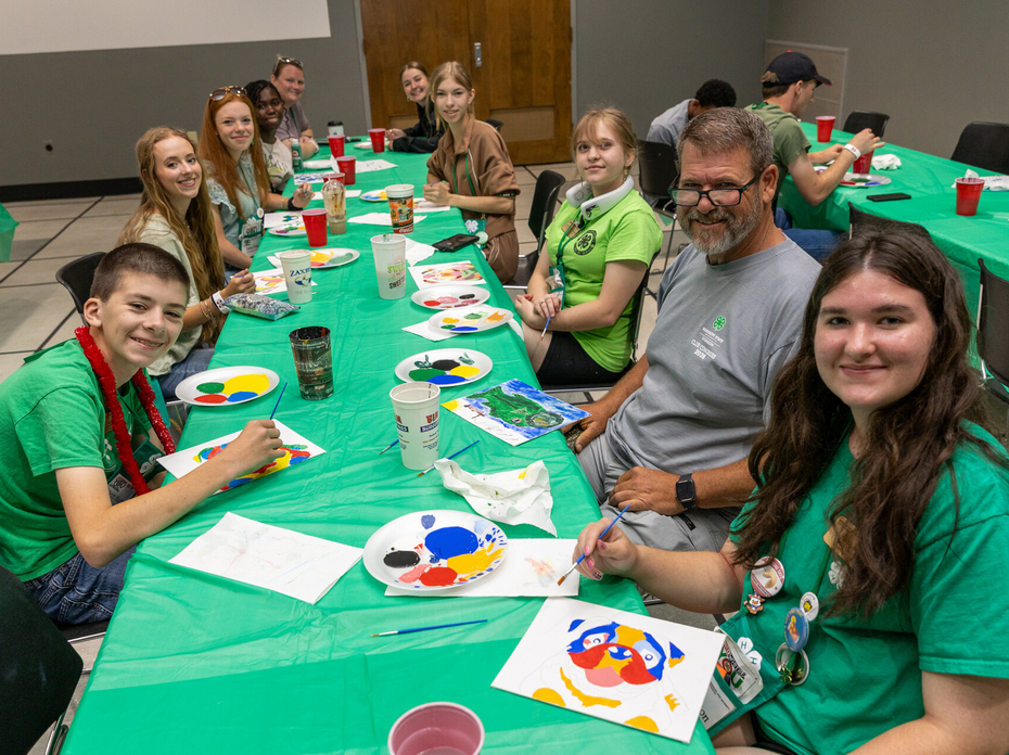 Teens smiling with an adult at a table full of painting supplies.