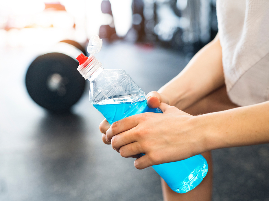 Closeup of hands holding a blue sports drink after a hard workout in the gym. 