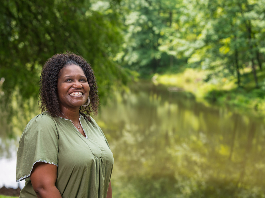 A person standing in front of a pond smiles at the sky.