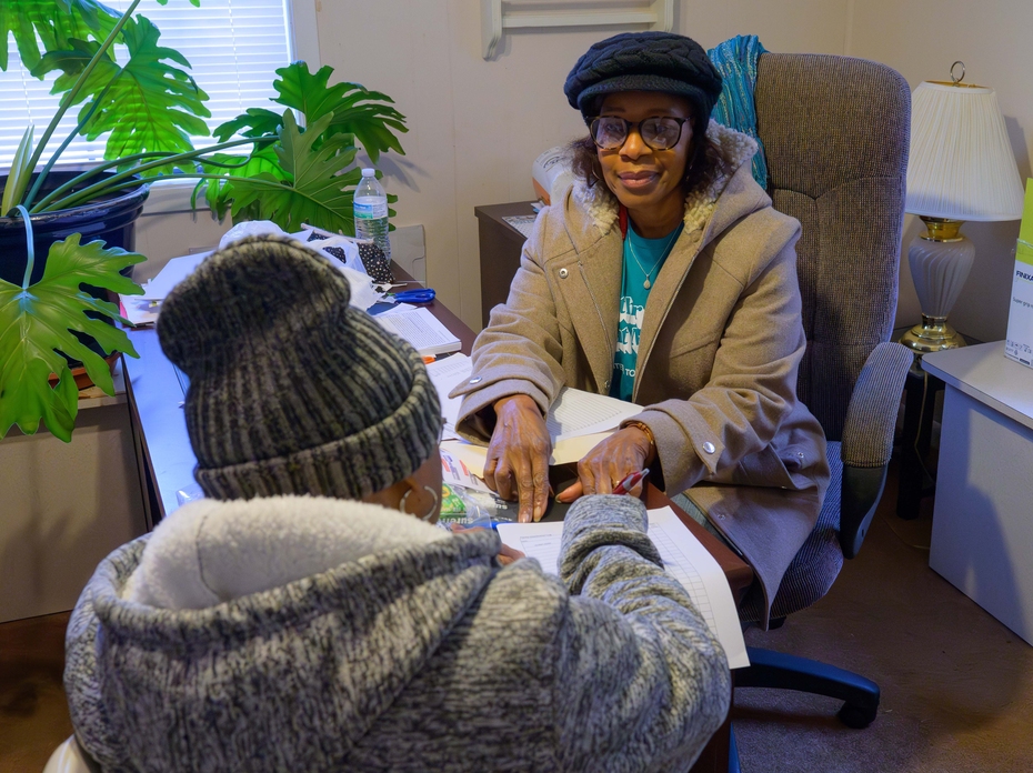 Two women face each other over a desk to review paperwork. 