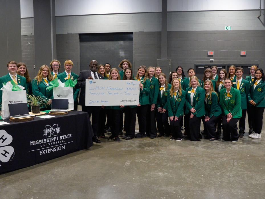 A large group of teenagers pose for a photo with a man holding a large presentation-style check.