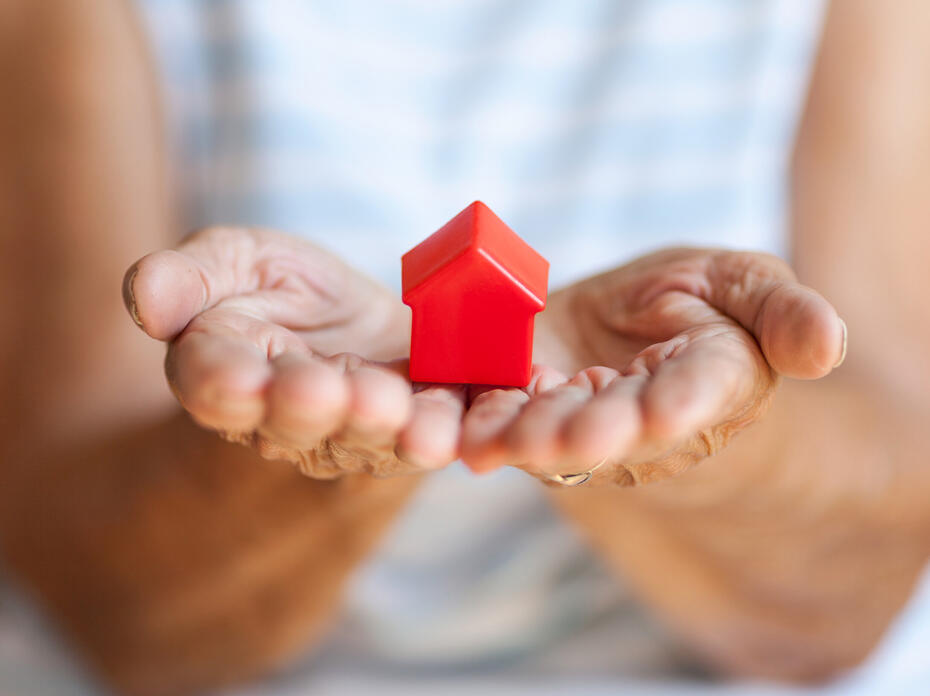 A small red toy house rests in a woman’s open hands.
