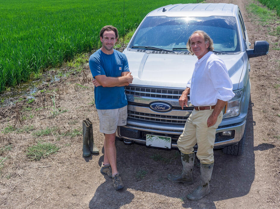 Two men standing in front of a pickup truck parked in a rice field.