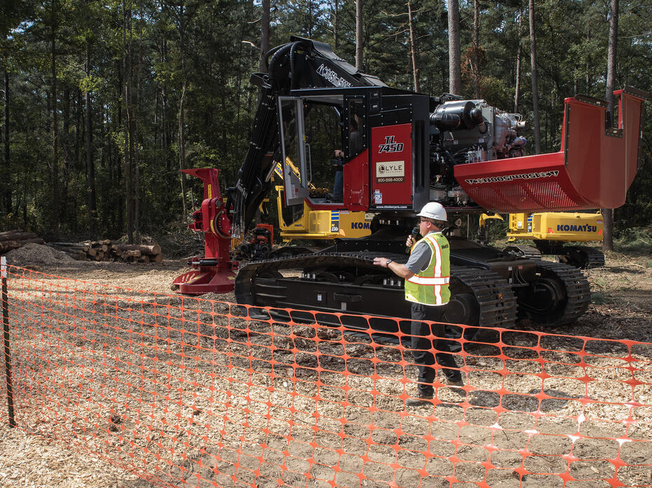 A man wearing a hard hat talking into a microphone in front of a piece of heavy equipment.