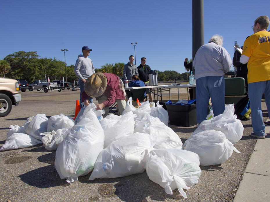 Person in straw hat tying up white trash bags.