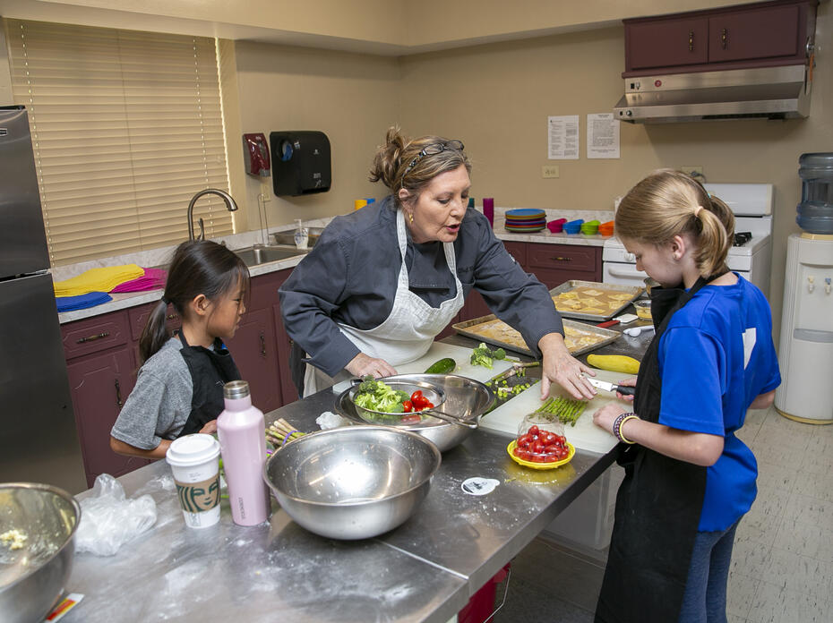  adult instructs two children in a kitchen setting.