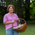 A smiling person standing outside and holding a basket full of colorful flowers.