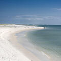 Dark blue water meets the edge of white sand on a clean, empty beach.