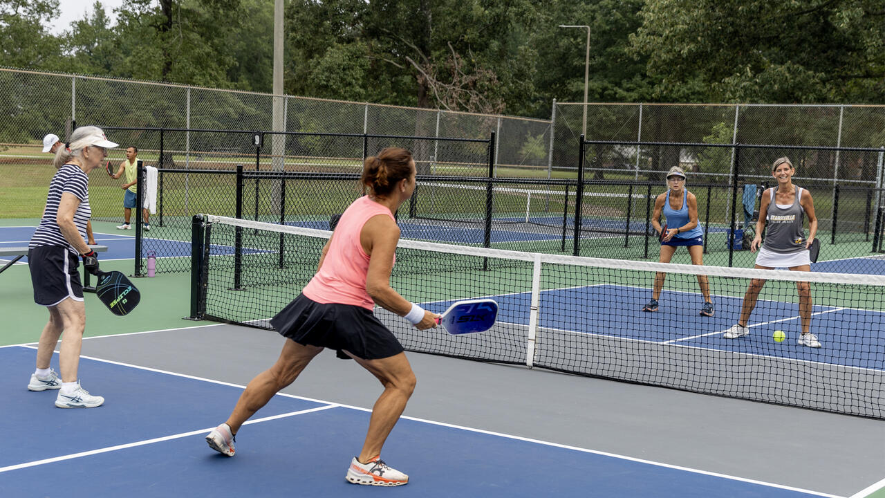 Four women holding paddles play a game on a court.