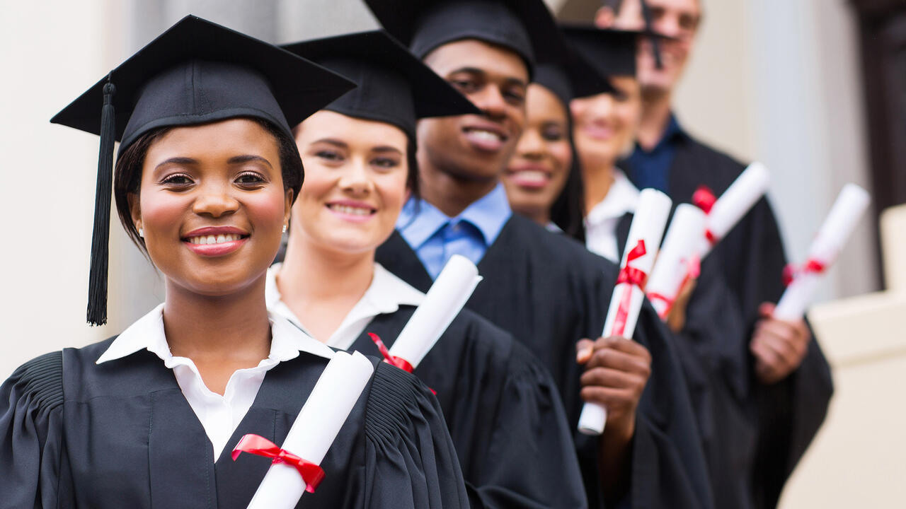 A group of smiling graduates pose in caps and gowns.