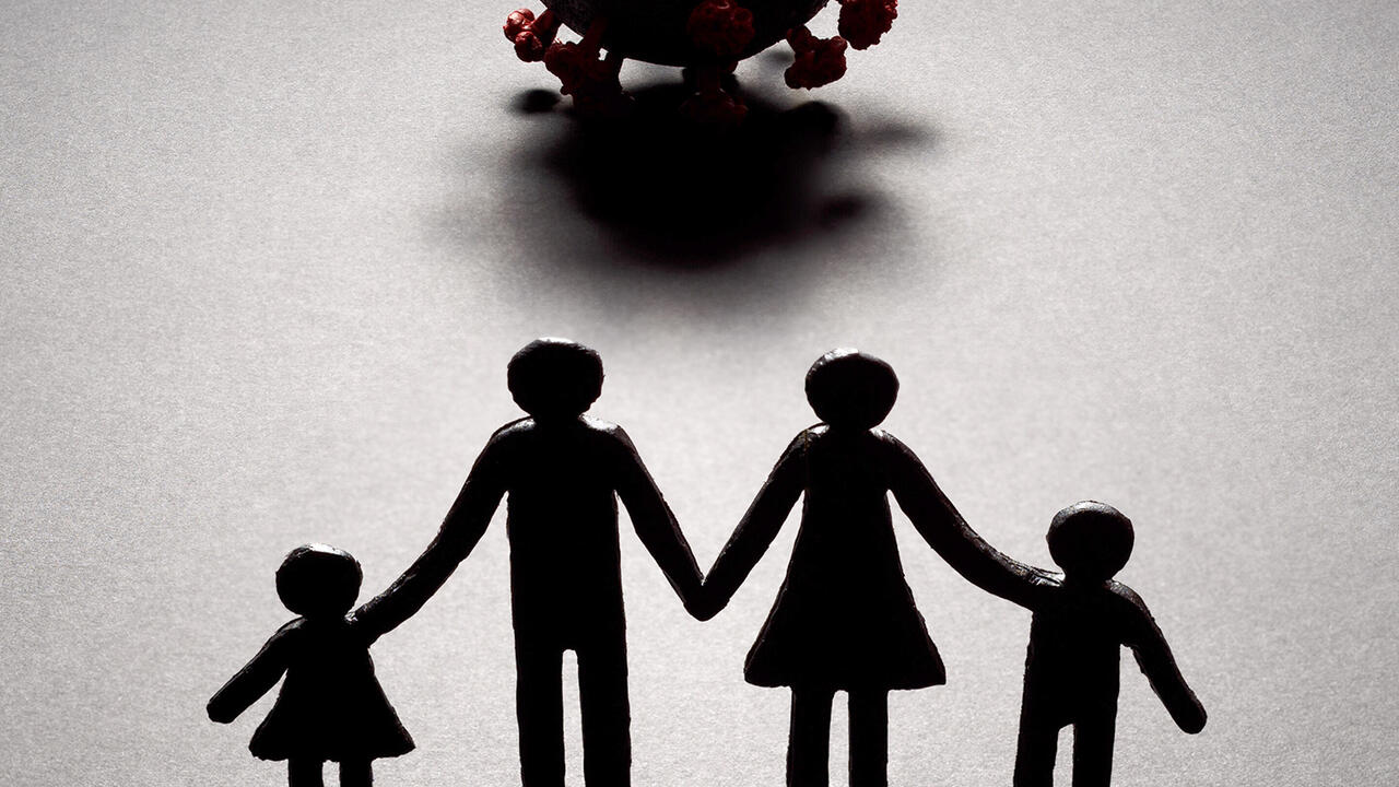 Silhouette of a paper cut-out style family of four facing a three-dimensional model of the novel coronavirus. 