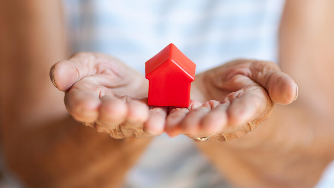 A small red toy house rests in a woman’s open hands.