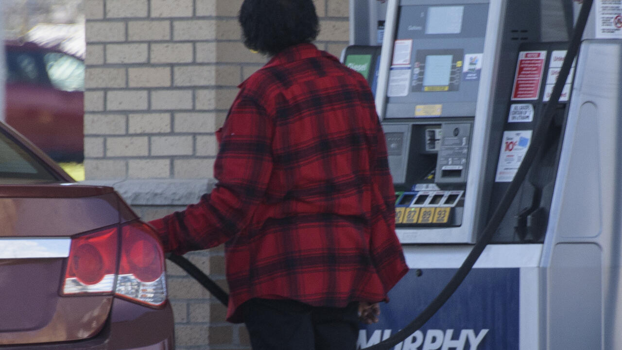 An adult pumps gas into a car at a gas station.