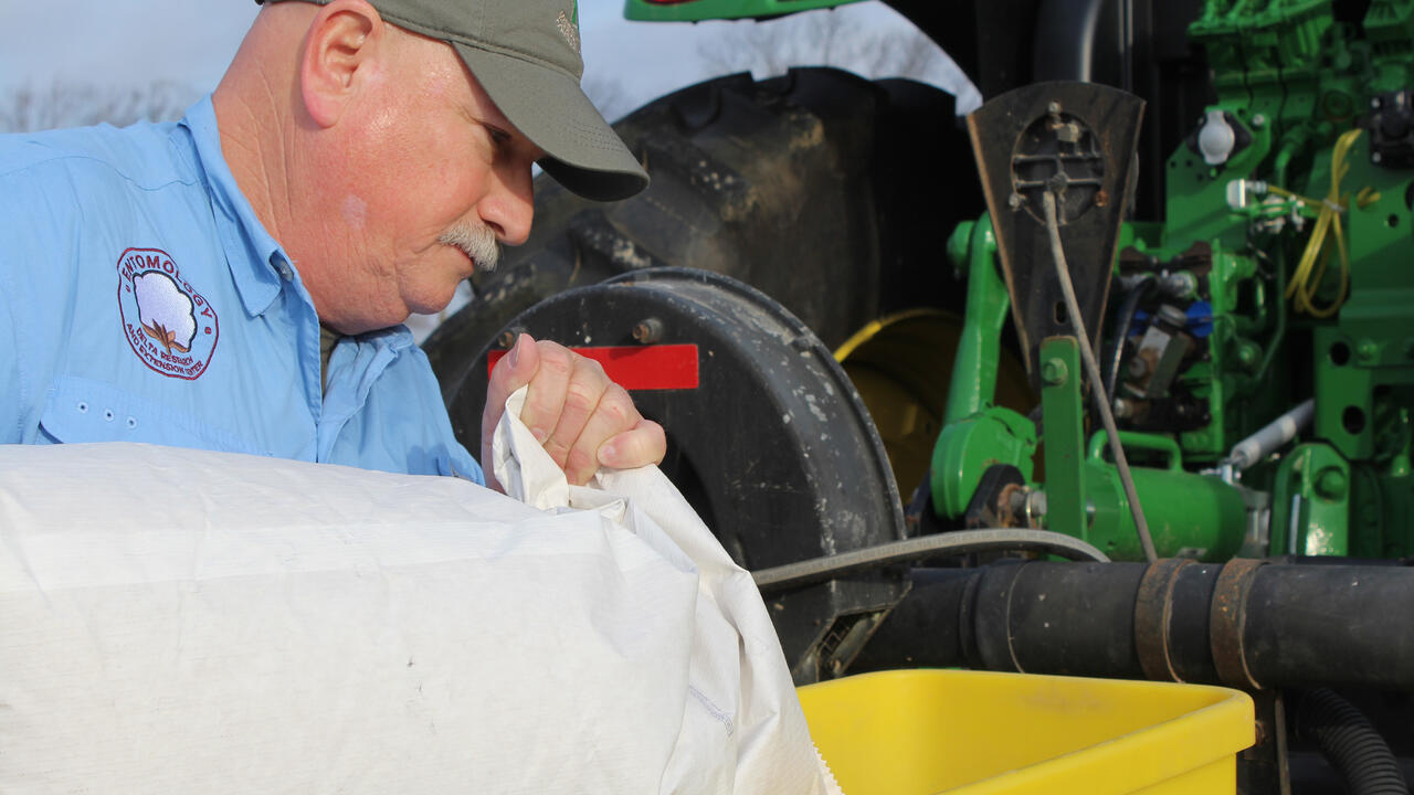 A man pours a bag into a yellow hopper on a tractor.