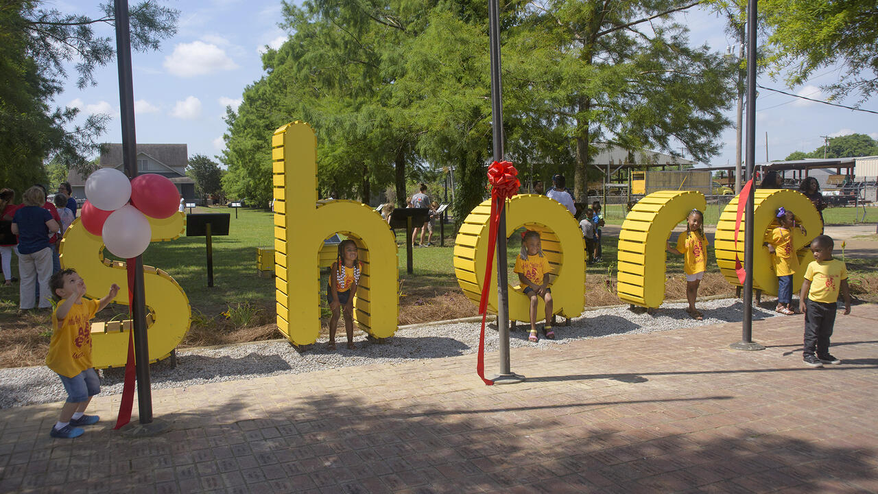 Children stand and sit around life-size, bright-yellow letters that spell out “share.”