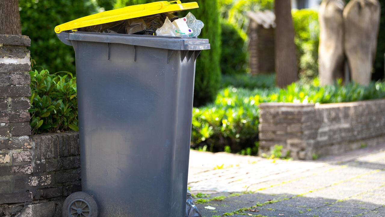 Full trash can sitting at the curb awaiting collection