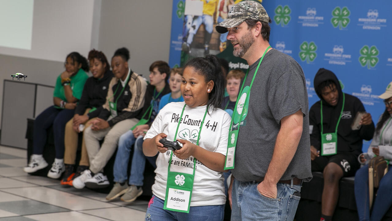 A man looks on as a child controls a remote for a drone.