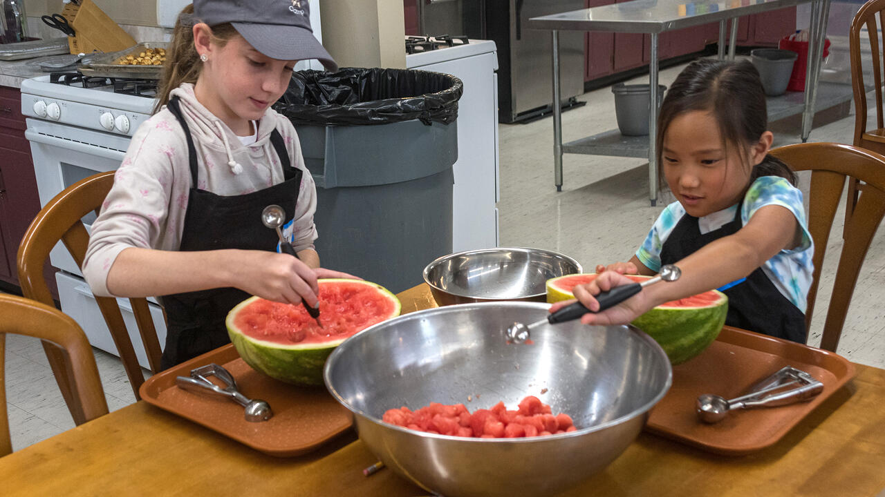 Two children make melon balls from a watermelon.