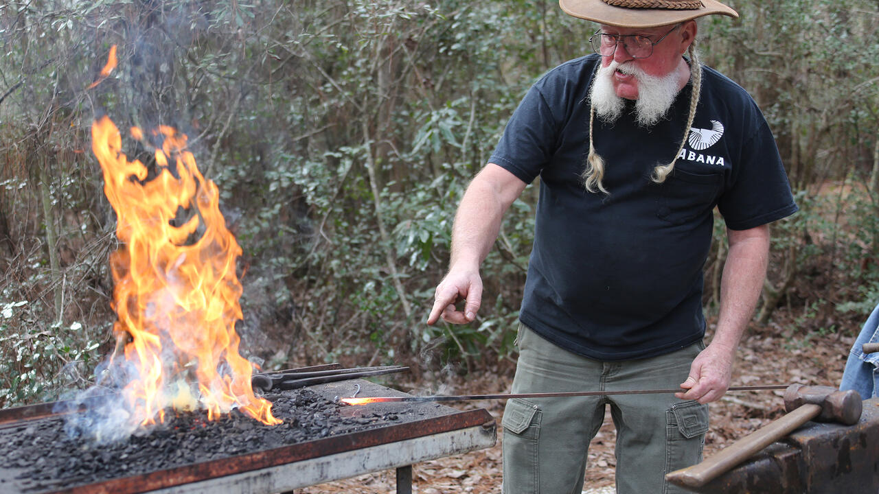 A man points at hot metal he just heated in a fire to forge it.