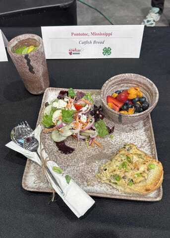 Catfish Bread, Creole Garden Salad and Fresh Fruit Salad is plated on a McCarty Pottery plate with a set of silverware wrapped in a napkin.