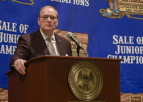 Mississippi State University President Mark E. Keenum speaks at a podium in front of a blue Dixie National Sale of Junior Champions backdrop.