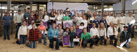 About 45 people, both adults and children, line up in roughly three rows. The prize winners are holding their award banners and checks. 