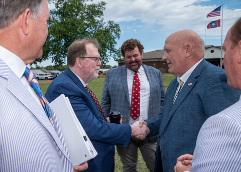 Two men shake hands as others look on.