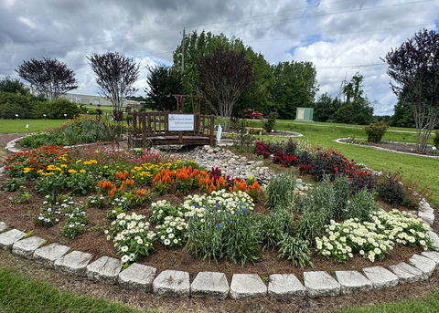 Garden stones line a circular flower bed full of colorful blooms in a landscape.