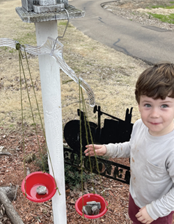 A plastic hanger with each notch holding three twine strings tied to a red bowl.
