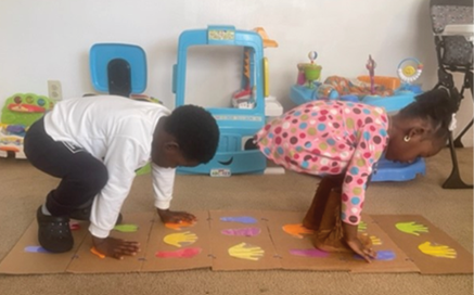 Two children follow the colorful hand and footprint patterns on cardboard.