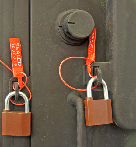 Two padlocks on a delivery truck door. Each lock has an orange tag with the word "sealed" followed by a seven-digit number. 