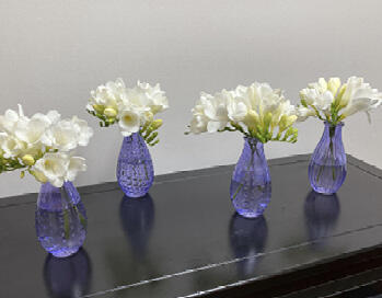 Four blue vases with small bouquets of white flowers spaced out on a rectangular table.