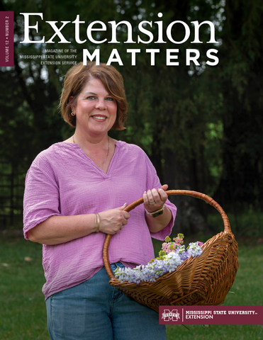 A smiling person standing outside and holding a basket full of colorful flowers.