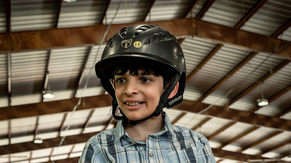 A smiling young man astride a horse and wearing a helmet.